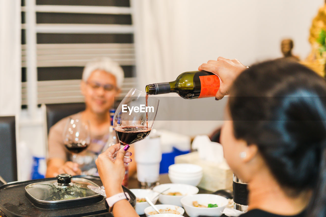 Woman hand pouring red wine into a glass from bottle at dinner party.
