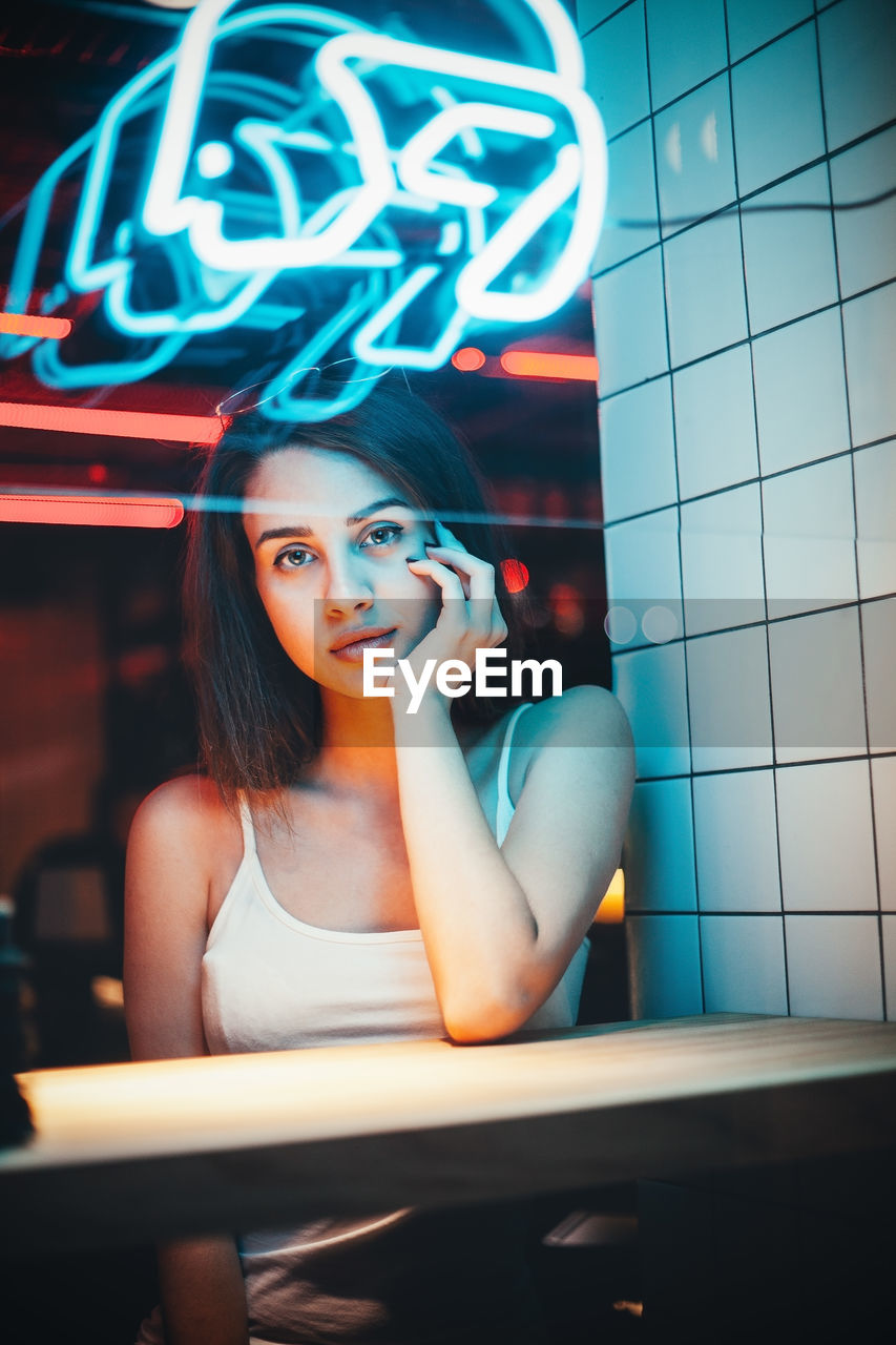 Portrait of young woman with hand on chin sitting in restaurant