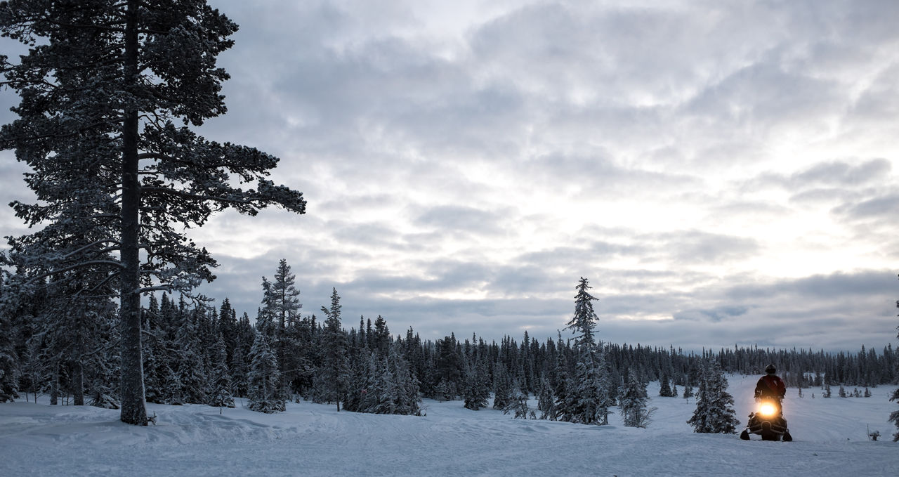 Man with vehicle on snowfield against sky during sunset