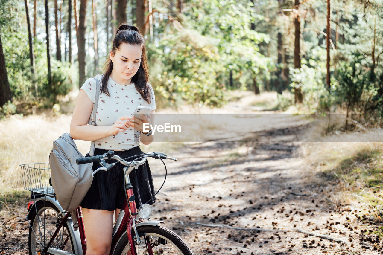 Best cycling apps. bike tracker. young woman with backpack riding bike and looking in cell phone on