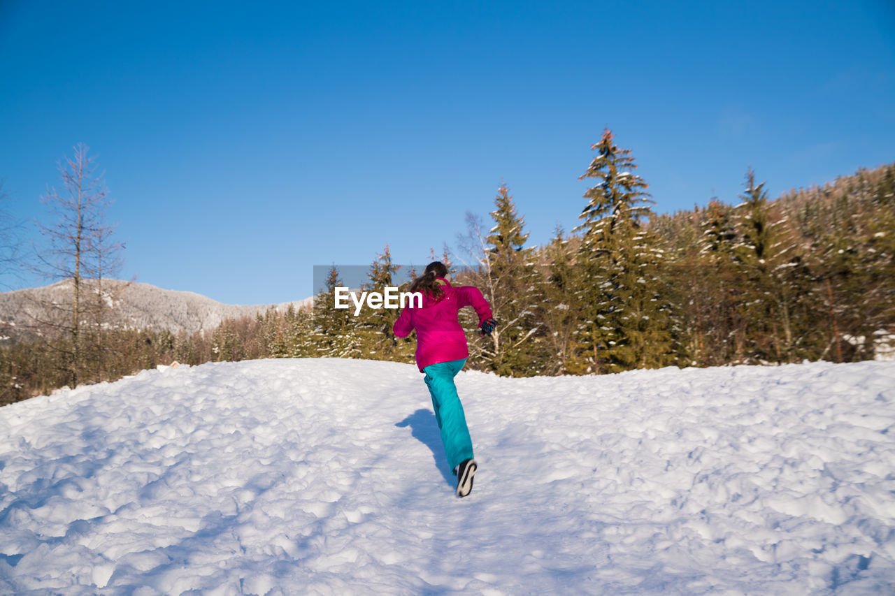 Rear view of girl running on snow covered land against sky