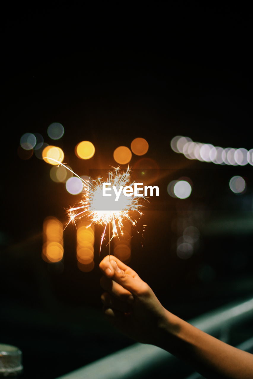 Hand holding illuminated firework display at night