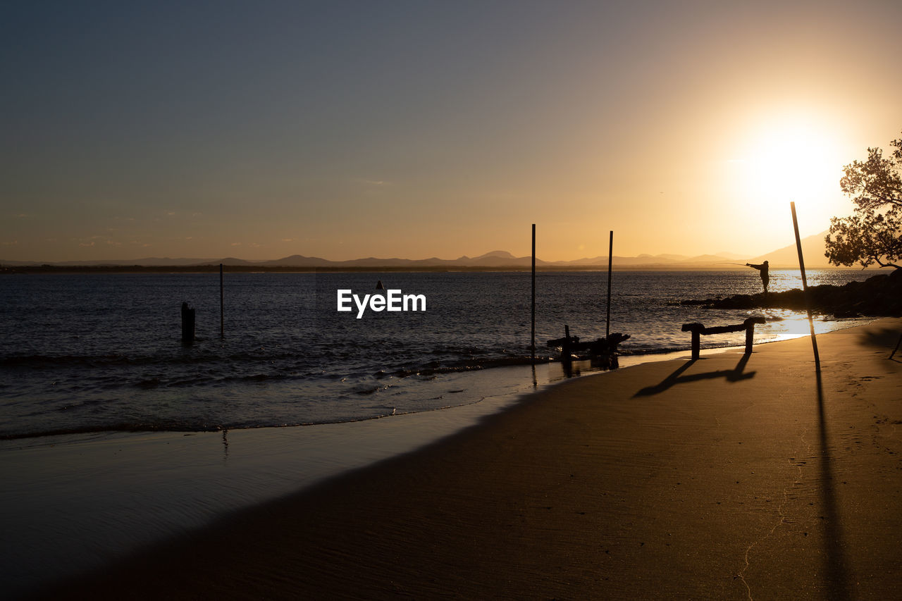 Scenic view of beach against sky during sunset with one people fishing