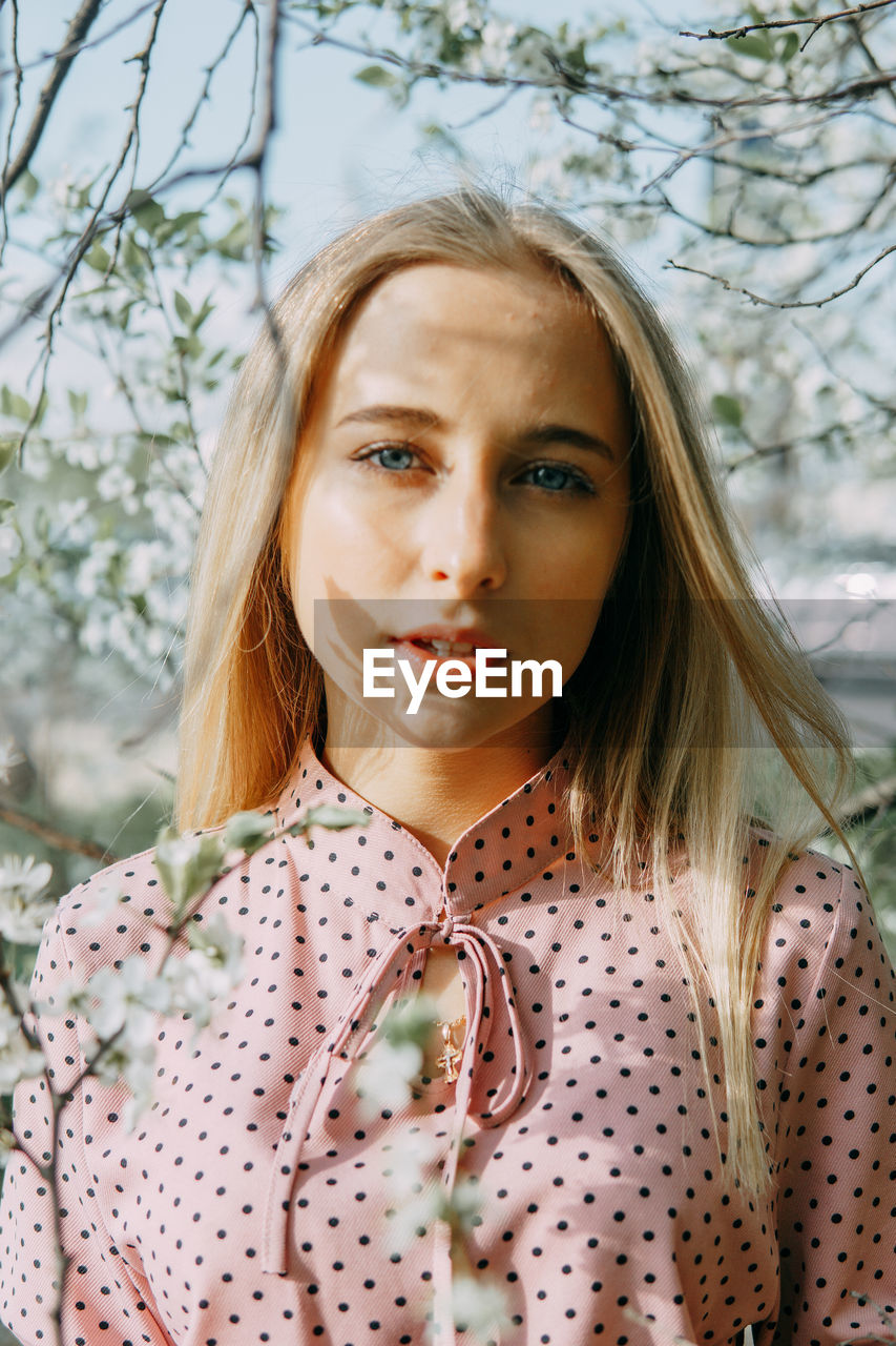 Blonde girl on a spring walk in the garden with cherry blossoms. female portrait, close-up. 