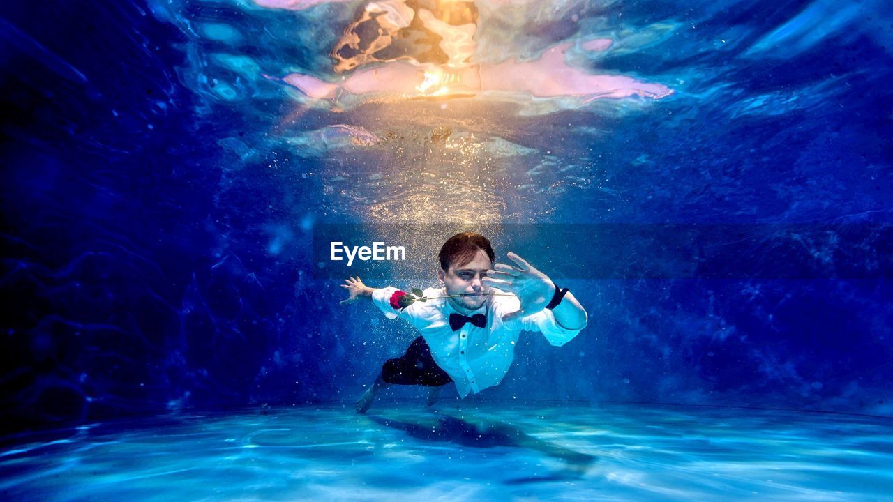 Full length of man carrying red rose in mouth while swimming in pool