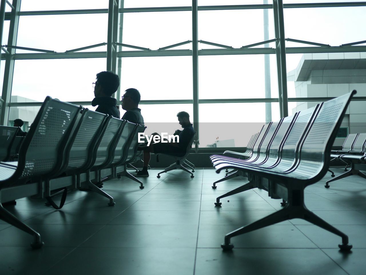 Men sitting on benches in waiting room at airport departure area
