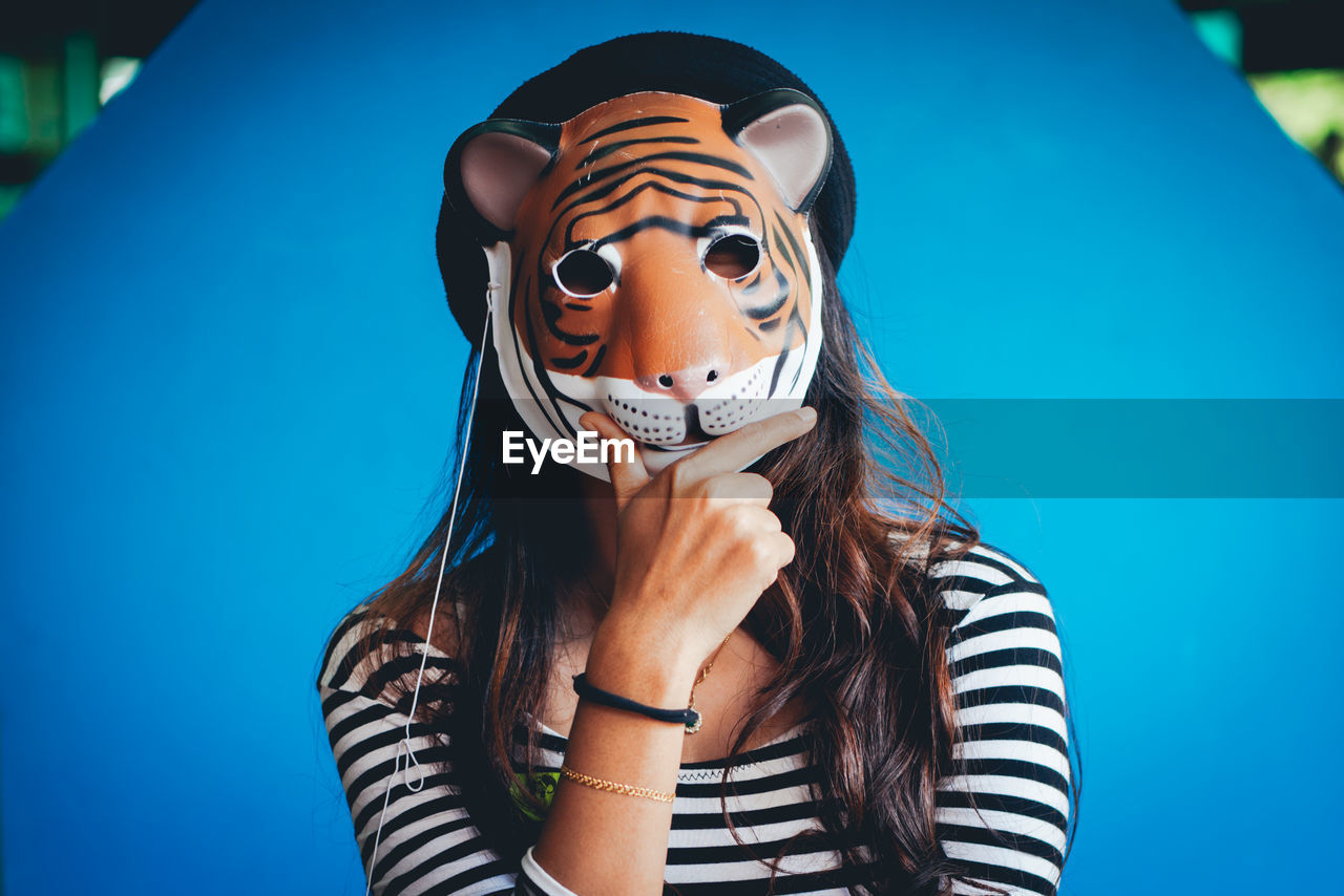 Portrait of woman wearing tiger mask against blue wall