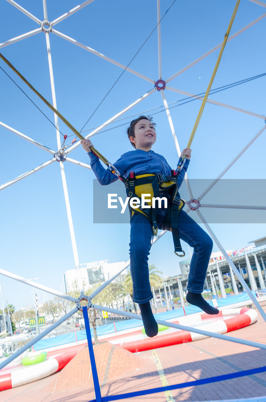 Low angle view of boy bungee jumping against clear sky