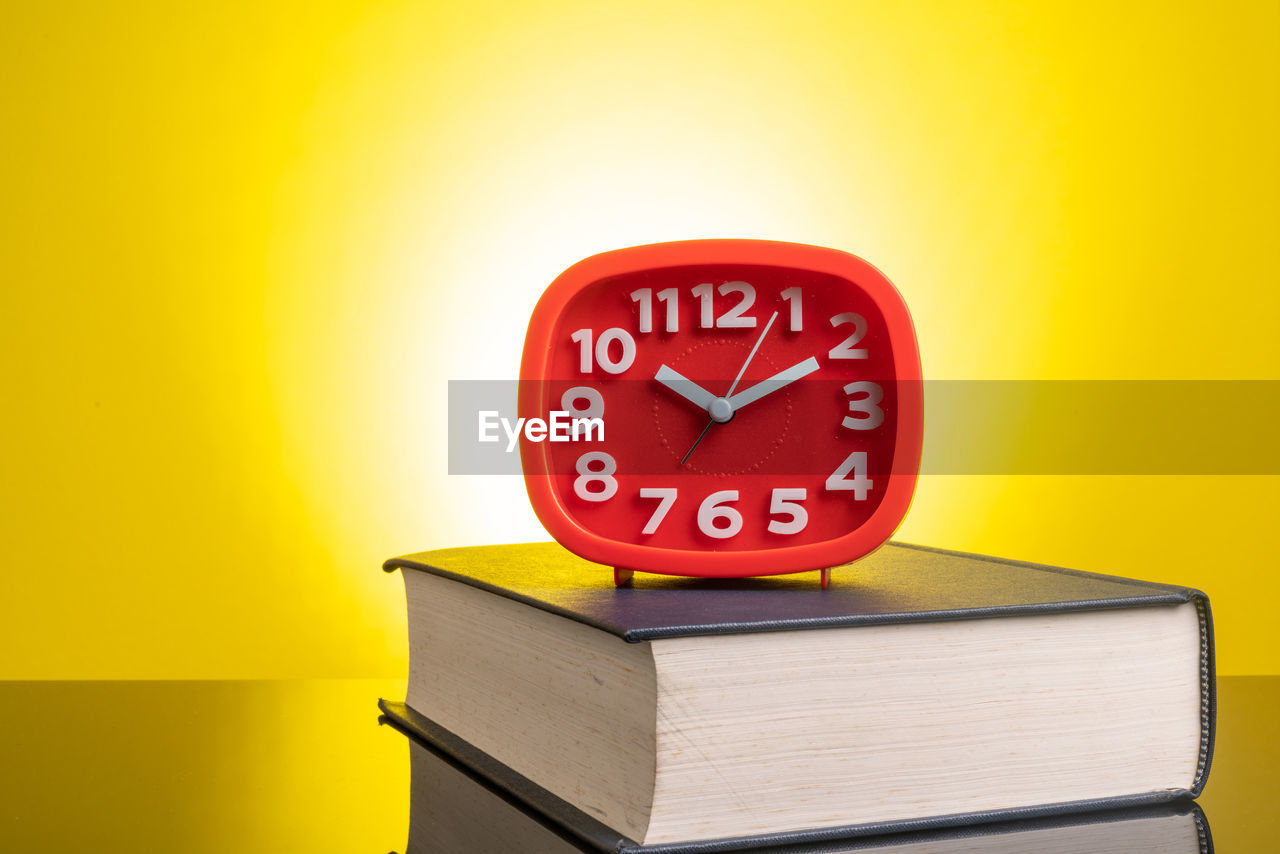 Close-up of clock and book against yellow background