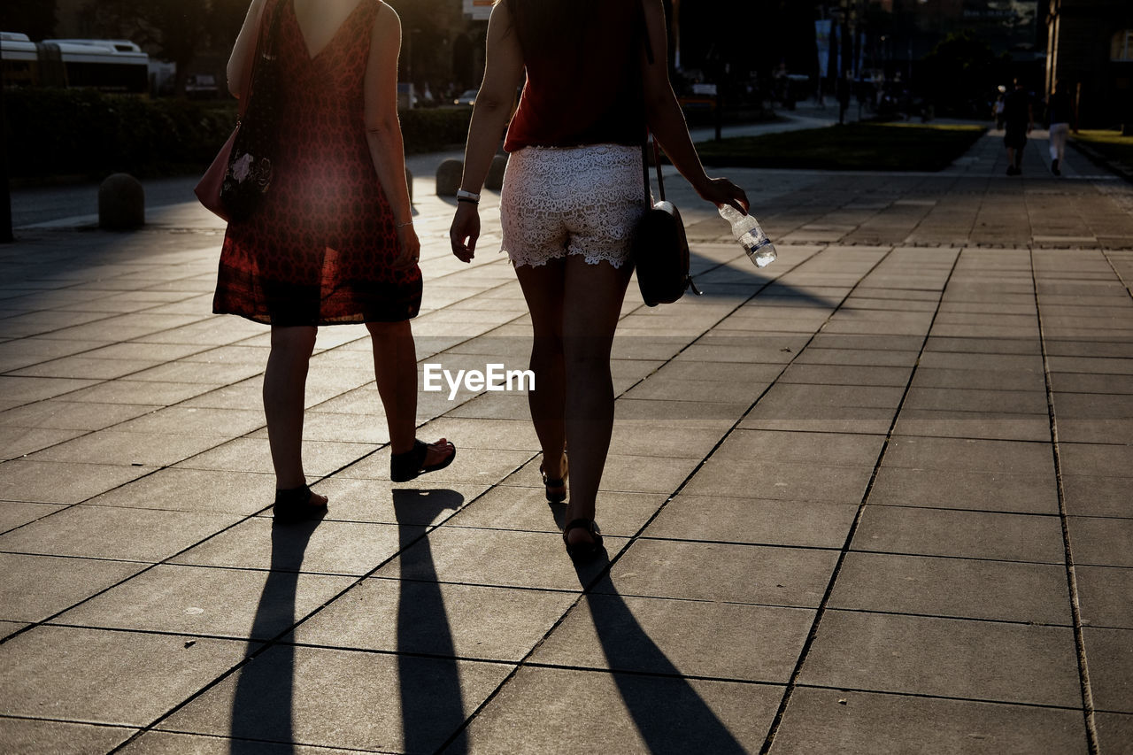 Low section of women walking on footpath in city during sunset