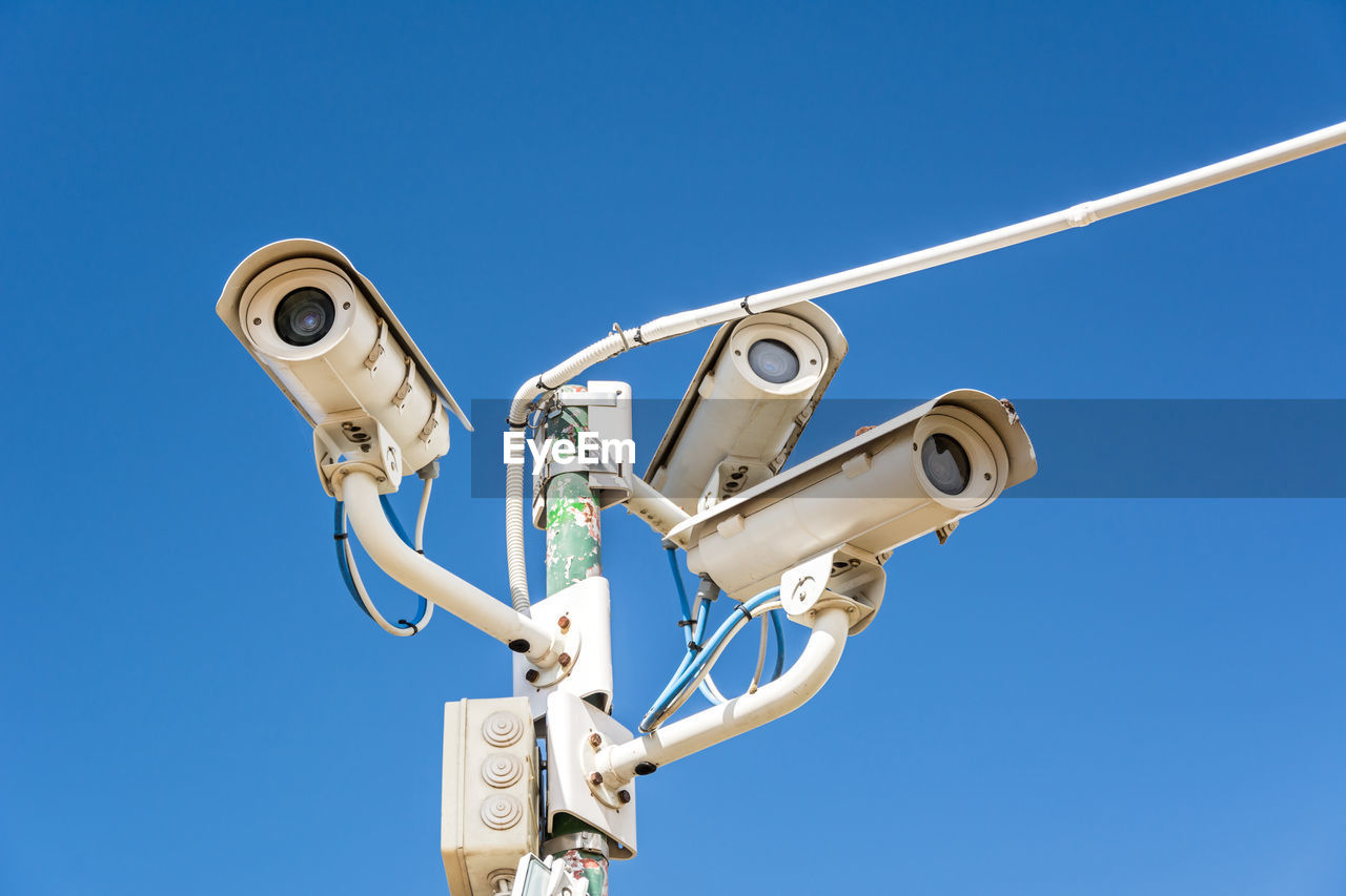 Low angle view of security cameras against clear blue sky