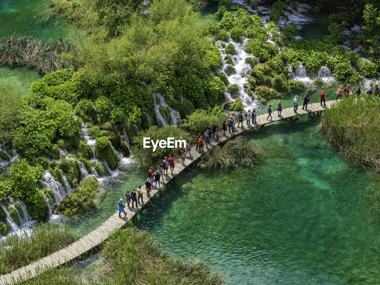 People crossing walkway above waterfall lakes