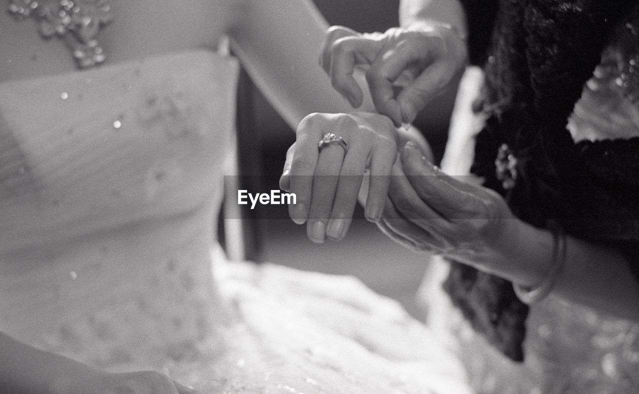 Cropped hands of bridesmaid tying thread on bride hand c during wedding