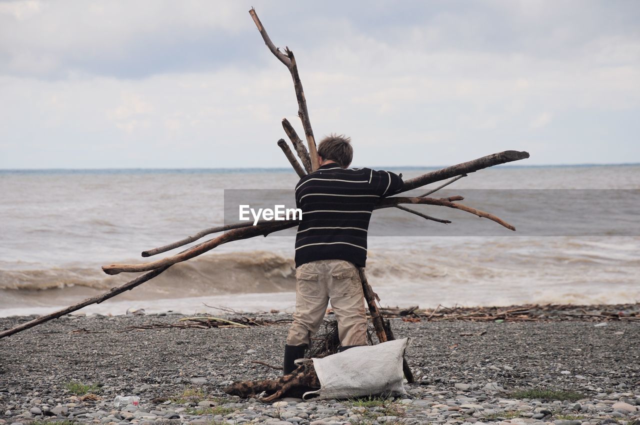 Rear view of man holding wood while standing at beach