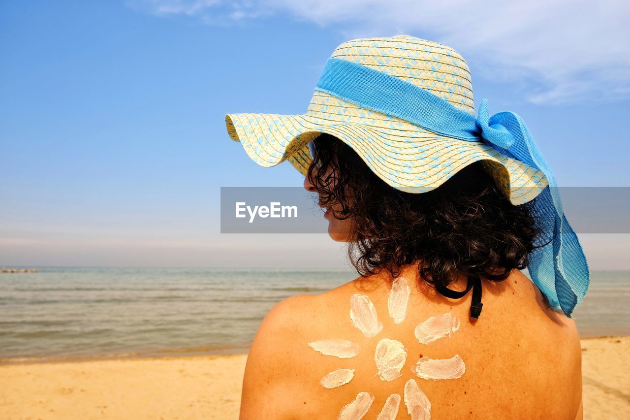 Rear view of woman in hat with suntan lotion on back at beach