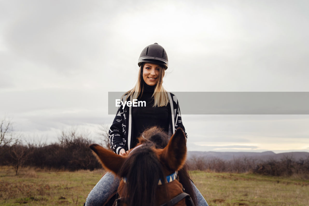 View of woman wearing helmet riding horses on field