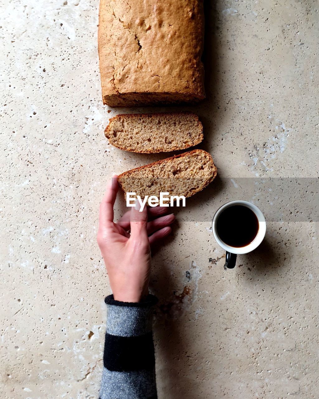Directly above shot of hand holding slice of bread with coffee on stone table