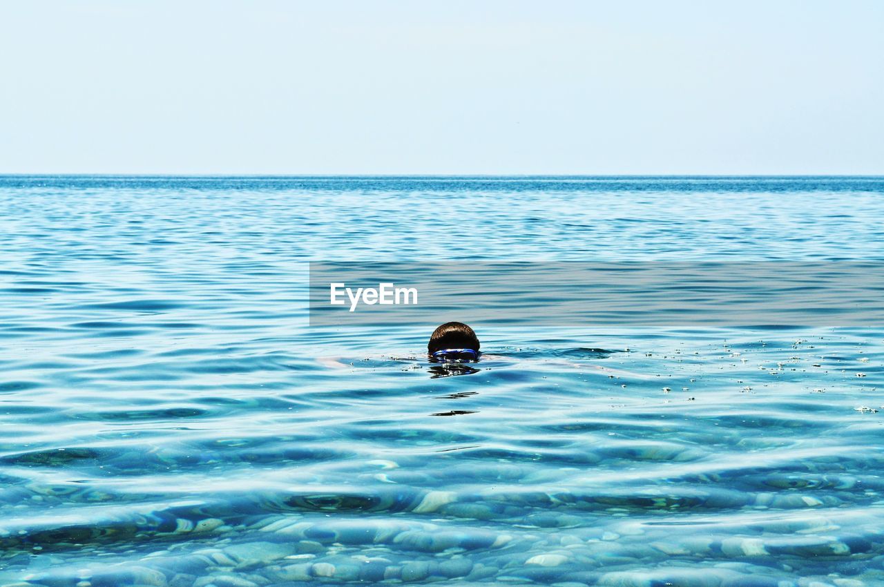 Man swimming in sea against clear sky