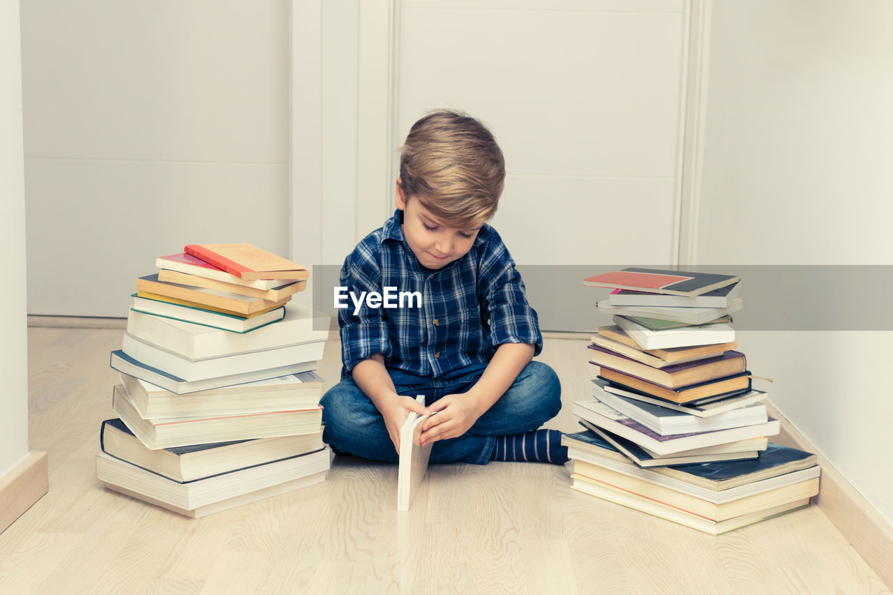 Small kid learning while sitting on the floor among heap of books.