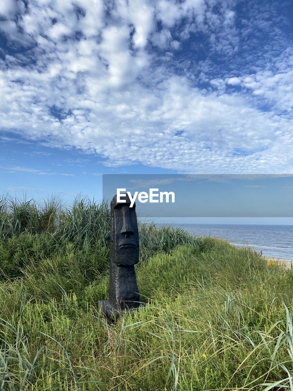 Wooden post on field by sea against sky