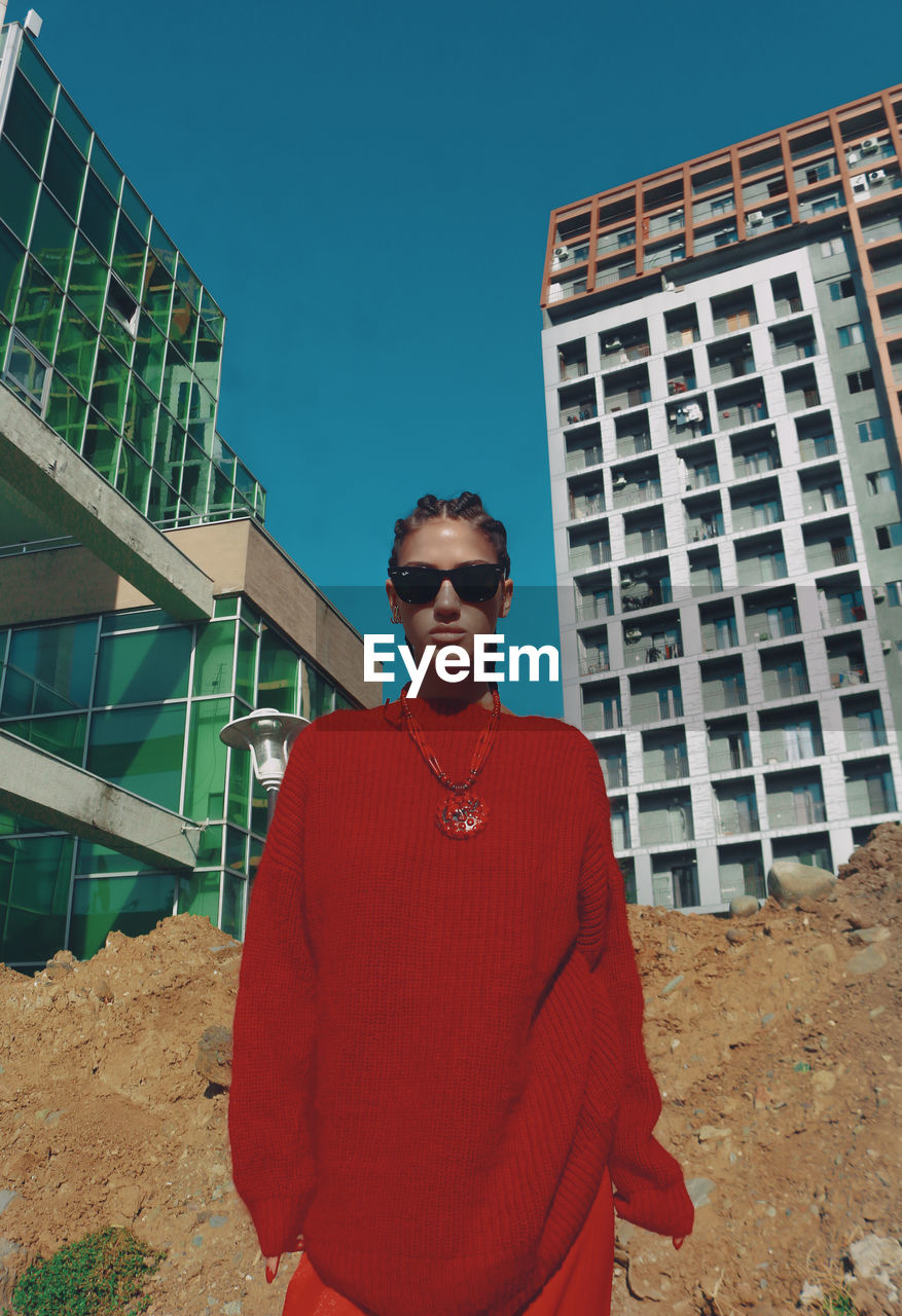 Portrait of young man wearing sunglasses standing against building