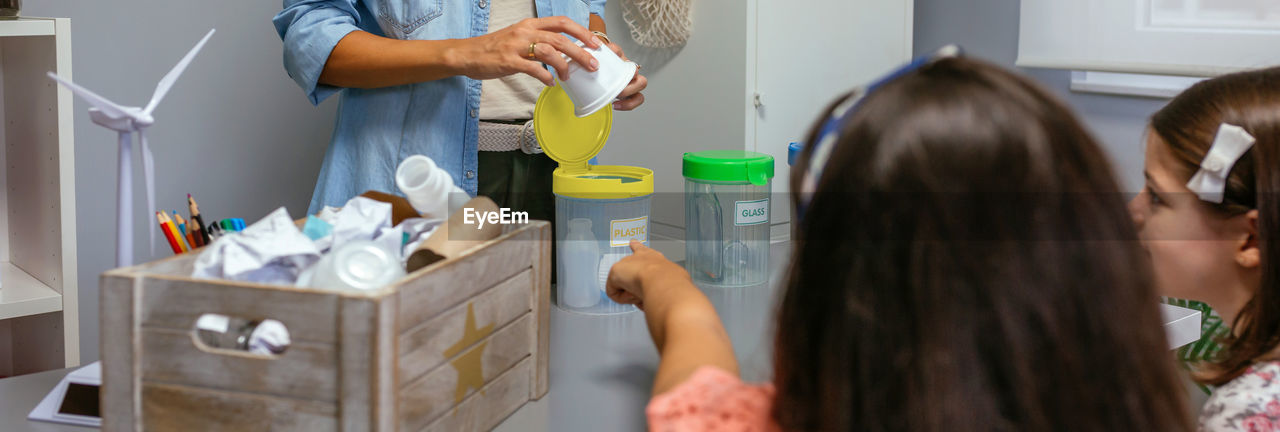 Girl pointing recycle box while female teacher holding plastic pack