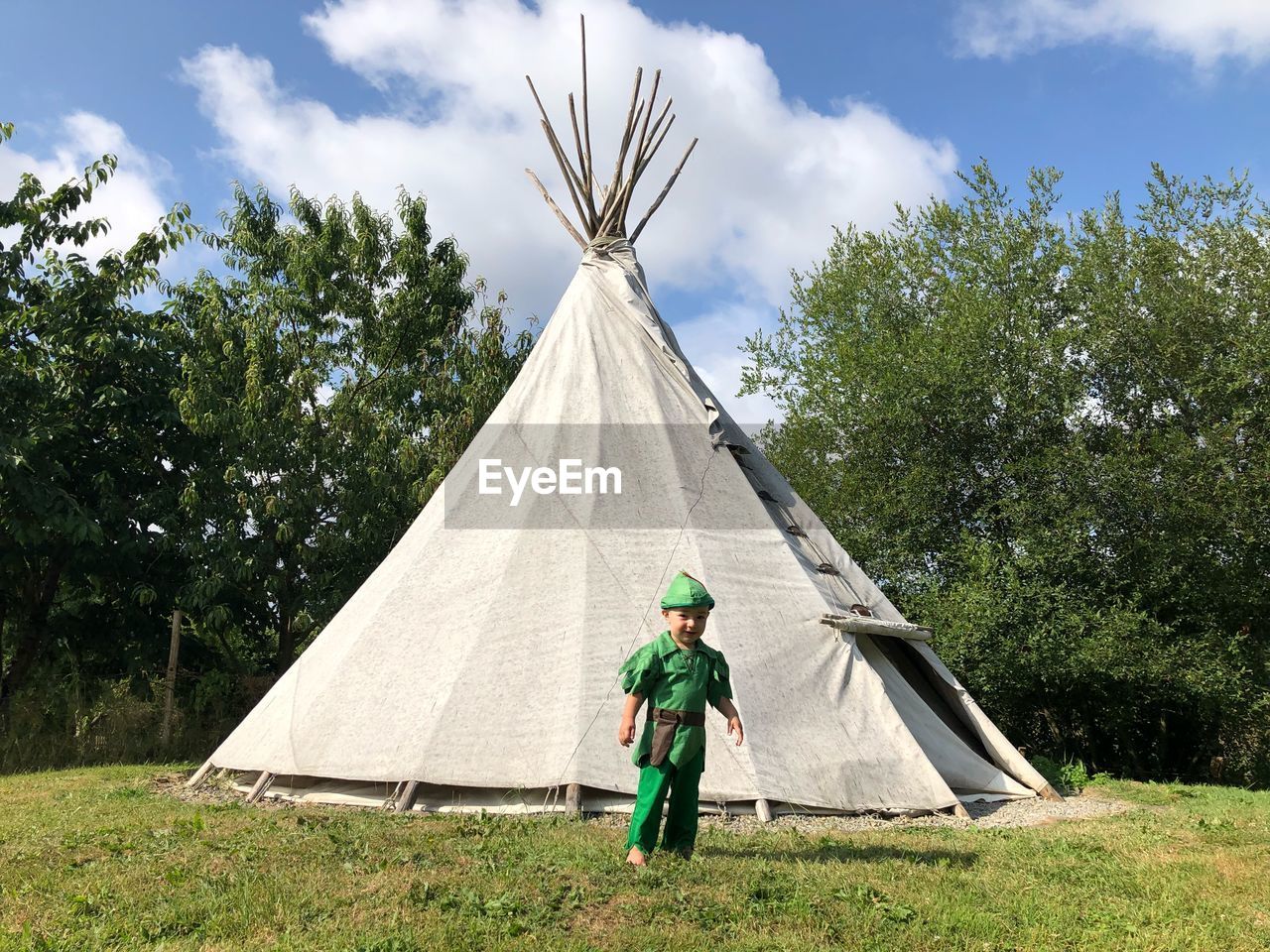 Boy standing against tent on field against trees