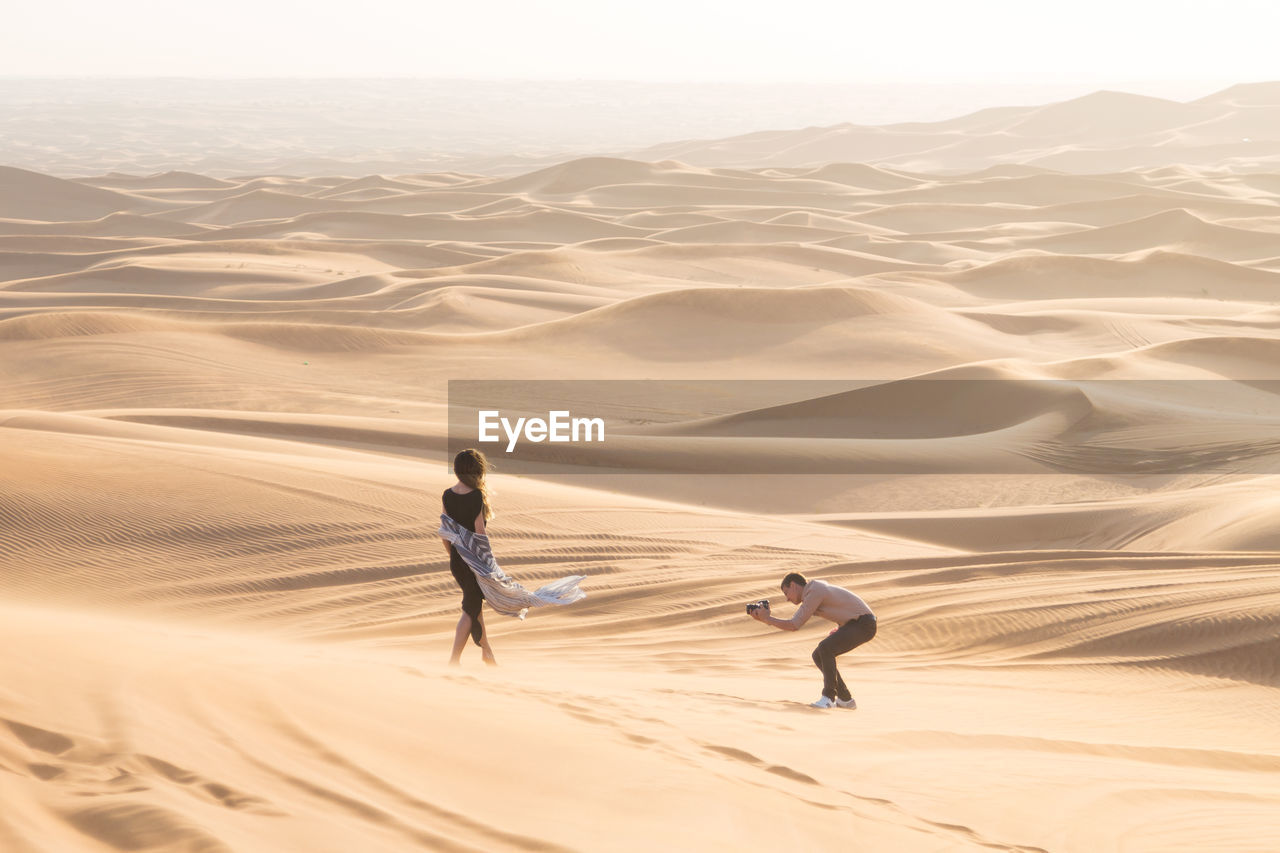 Man photographing woman standing at desert