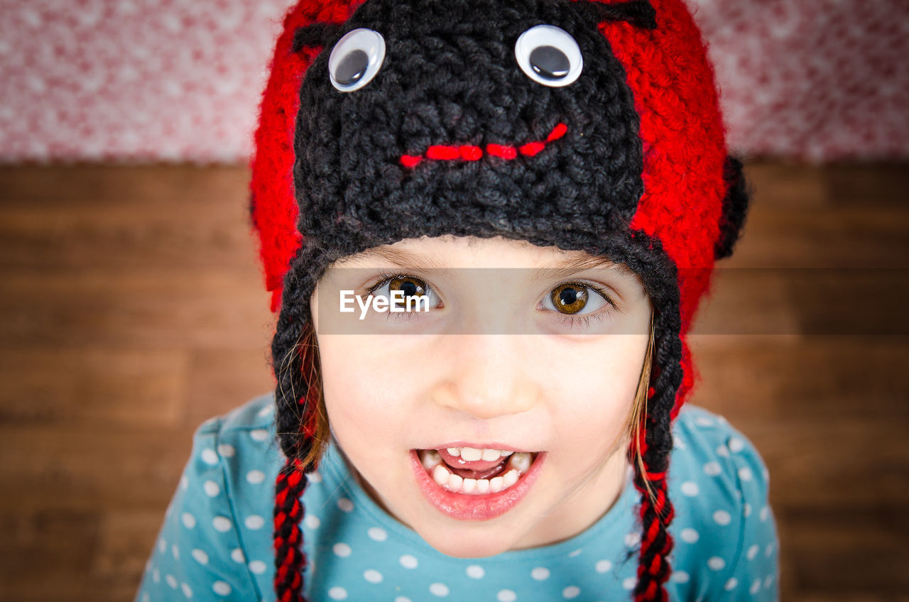 High angle portrait of smiling girl wearing knit hat standing on hardwood floor at home