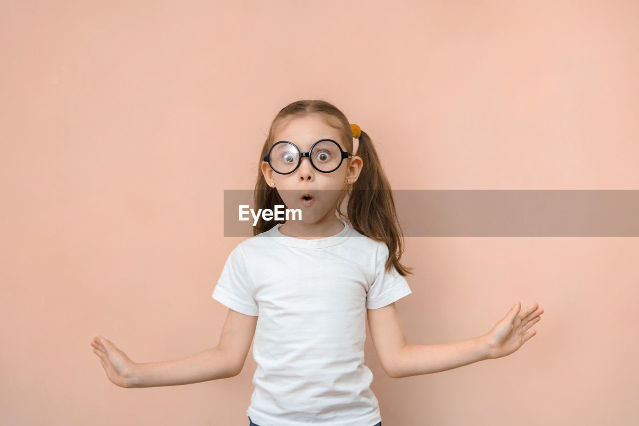 childhood, child, one person, eyeglasses, studio shot, women, female, glasses, portrait, cute, indoors, colored background, copy space, fun, emotion, human face, waist up, white, skin, happiness, standing, looking at camera, photo shoot, casual clothing, hairstyle, front view, toddler, smiling, person, vision care, pink, humor, facial expression, innocence, lifestyles, positive emotion, cut out, adult