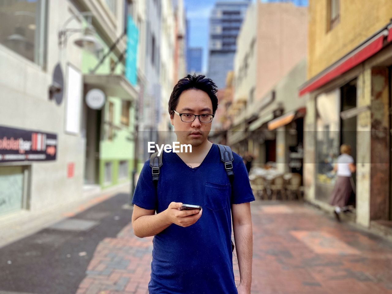 Portrait of young asian man using mobile phone in laneway against buildings in the city.