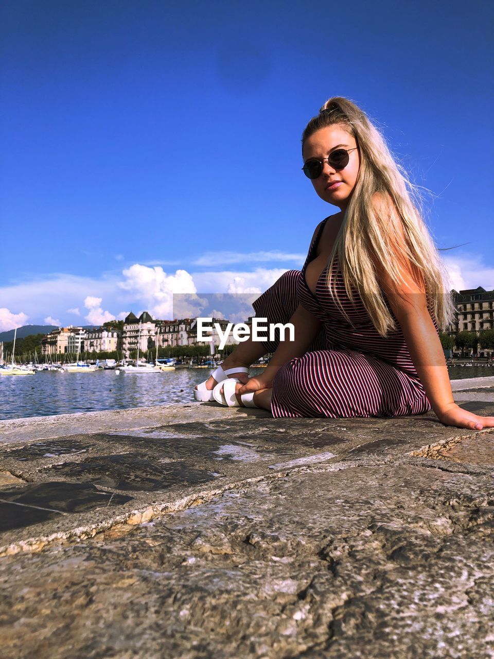 Portrait of woman wearing sunglasses while sitting by river against sky