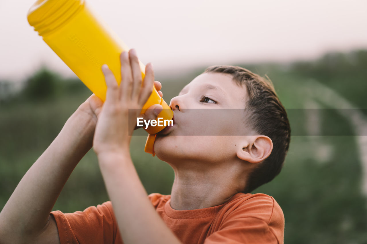 A child drinks water from a orange bottle