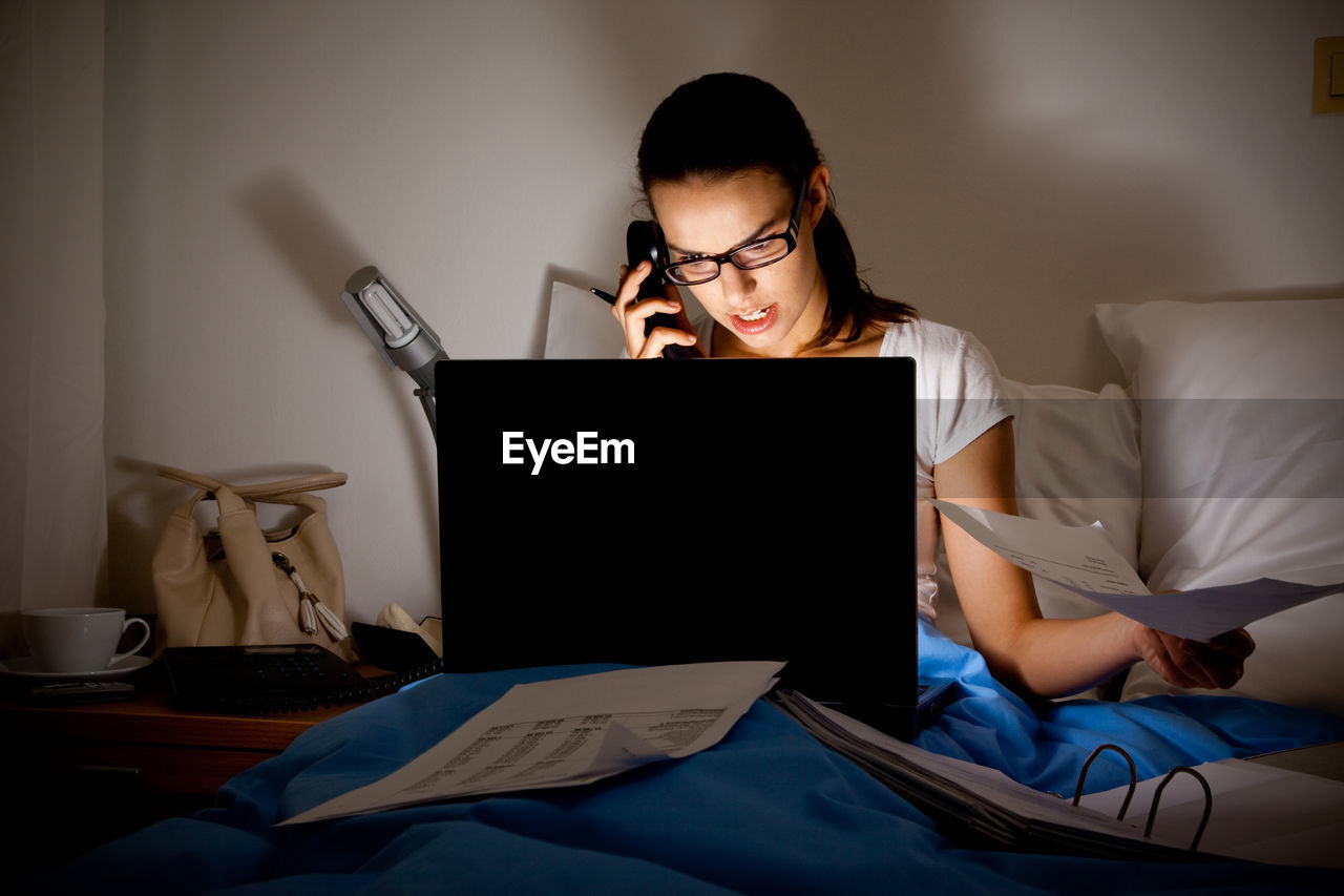 Angry woman talking on telephone while using laptop on bed at home