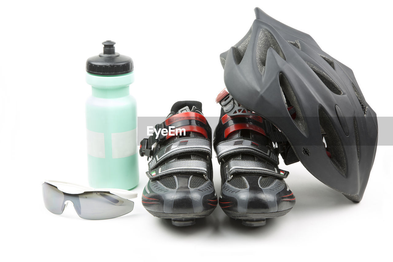 Close-up of cycling helmet leaning on sports shoes by sunglasses and water bottle against white background