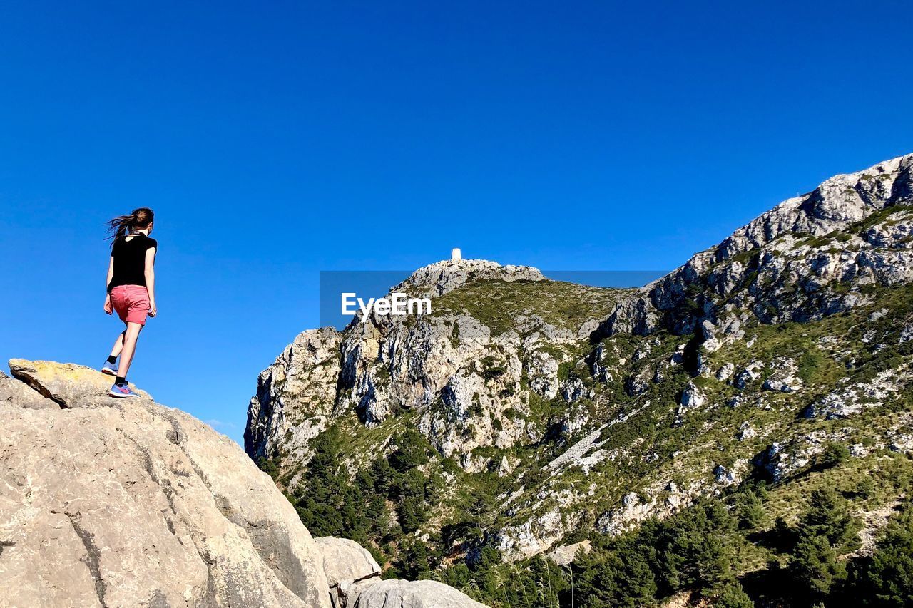 LOW ANGLE VIEW OF MAN ON ROCKS AGAINST BLUE SKY