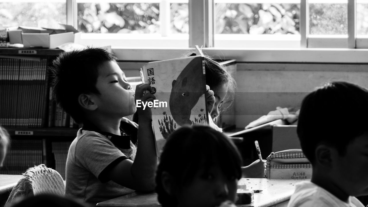 Cute boy reading book while making face in classroom