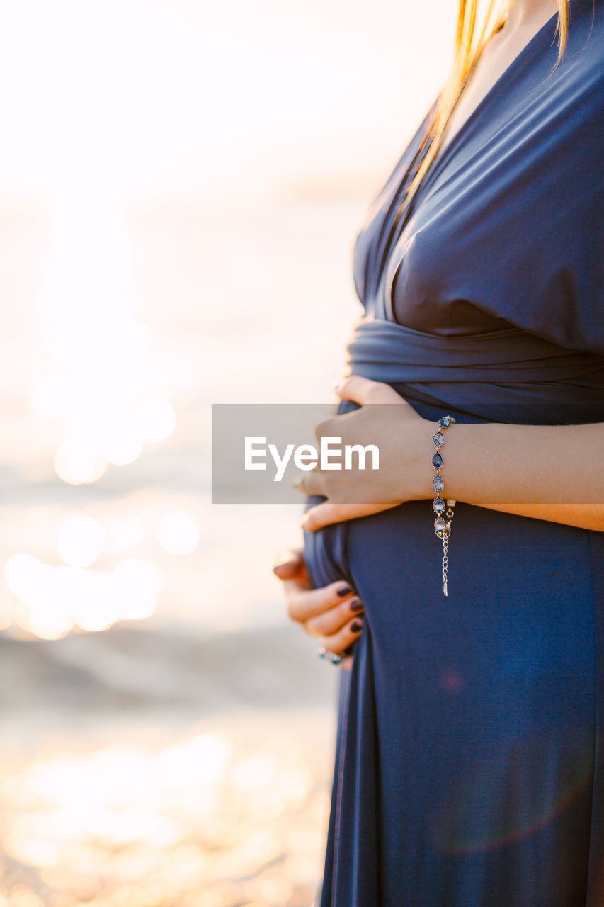 Side view of pregnant woman standing at sea shore against sky