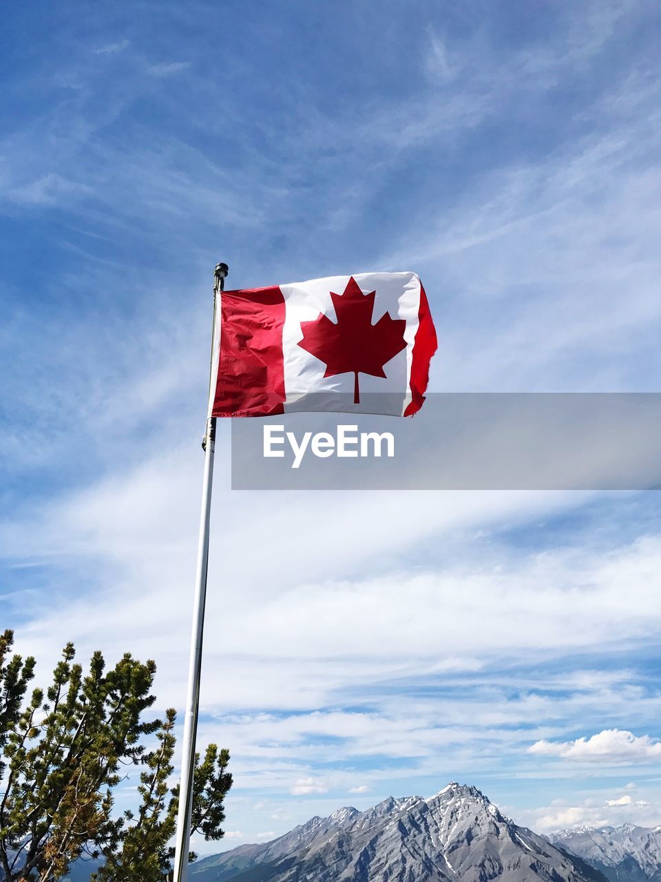 Low angle view of canadian flag waving with mountain in background against sky