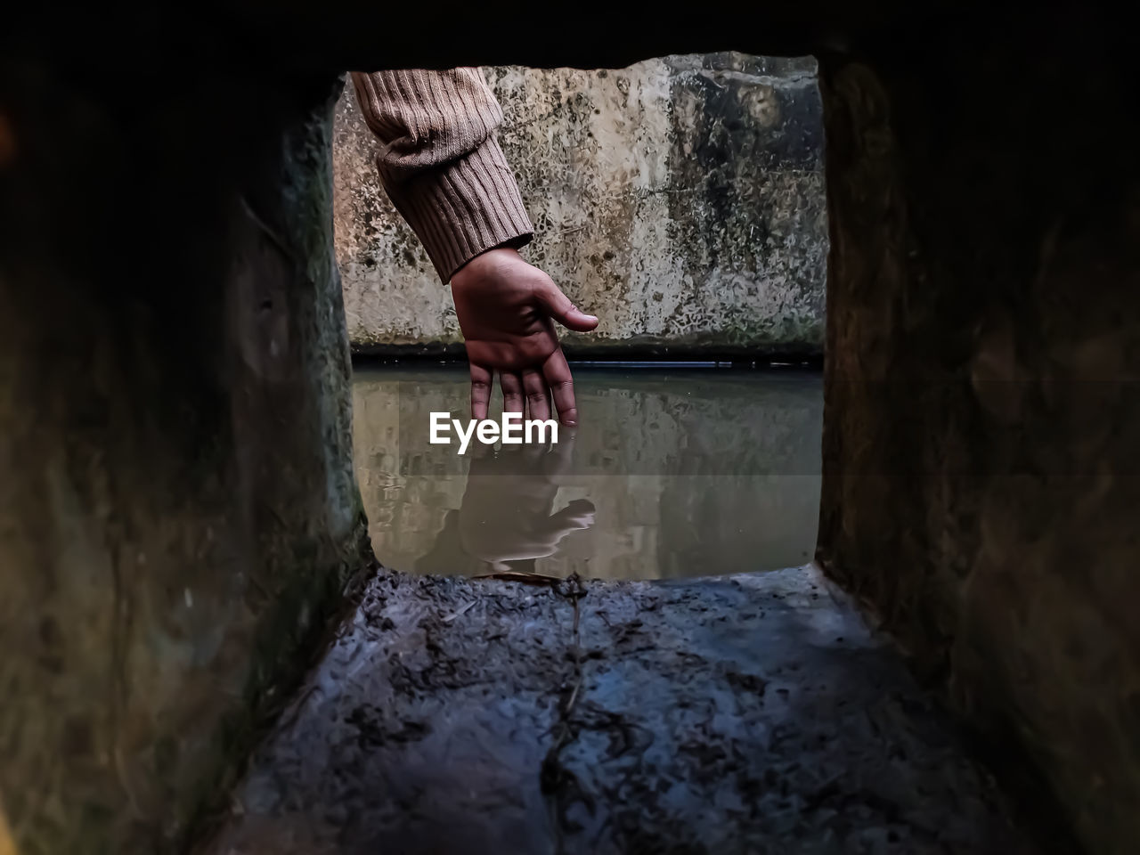 The reflection of a girl's hand fellon a water-filled cistern.