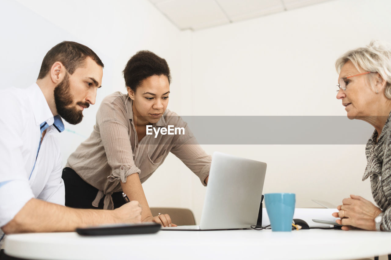 Businesspeople using laptop at table in office