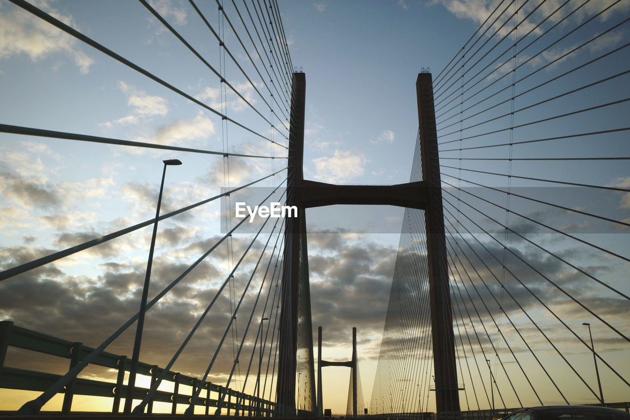 LOW ANGLE VIEW OF SUSPENSION BRIDGE AGAINST SKY DURING SUNSET