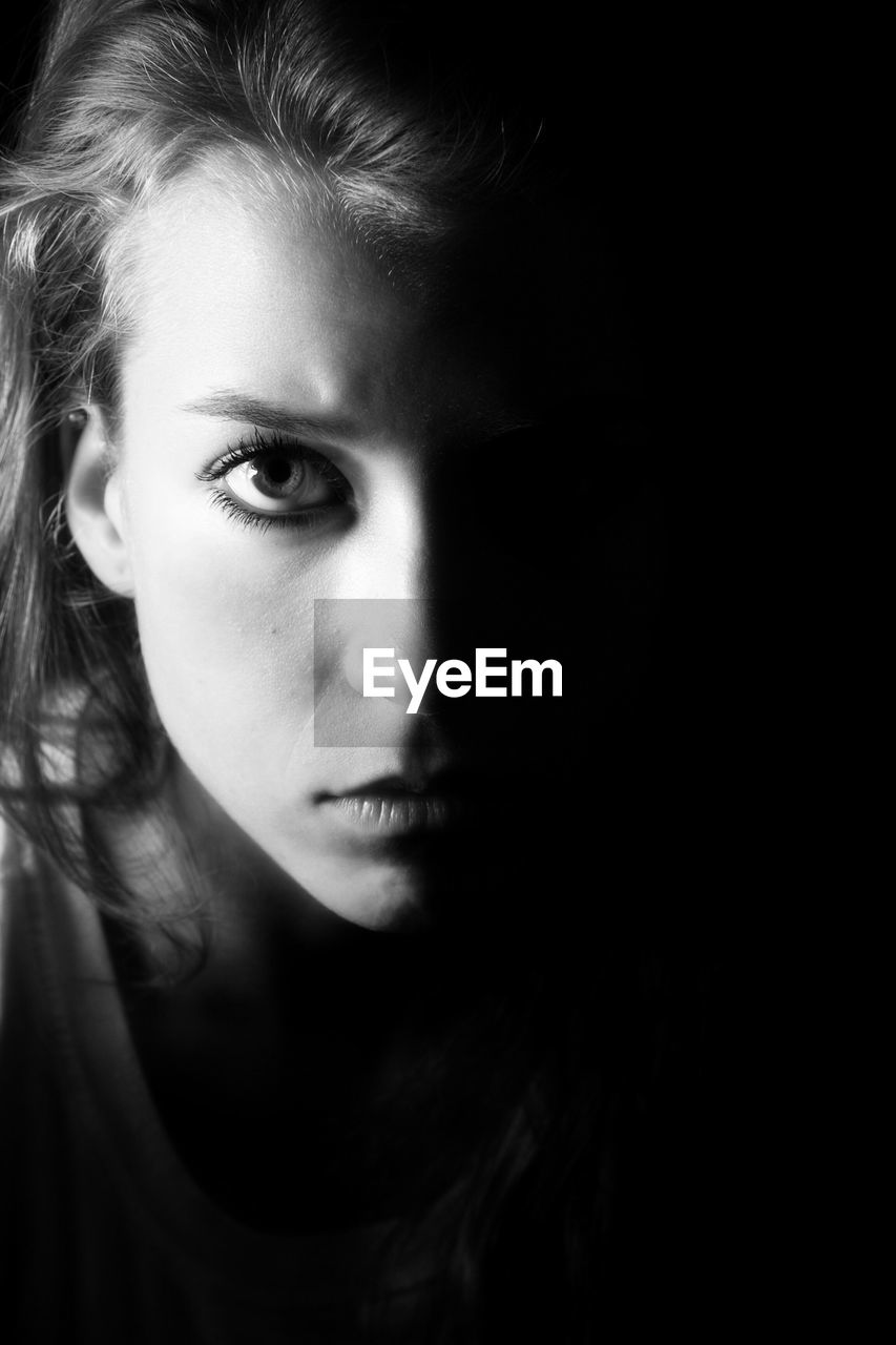 Close-up portrait of serious beautiful woman against black background