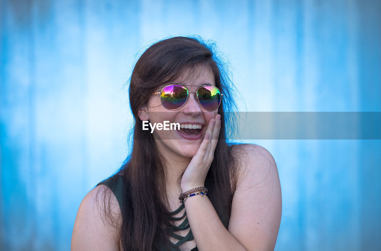 Portrait of happy woman wearing sunglasses while standing against wall