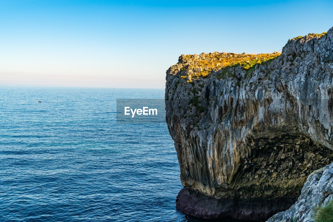 Rock formation in sea against clear blue sky