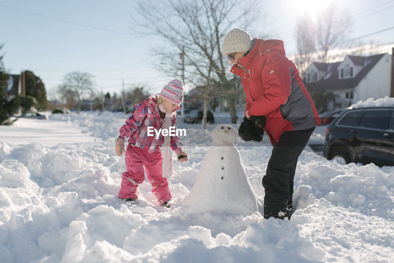 Grandmother and granddaughter building snowman in front yard
