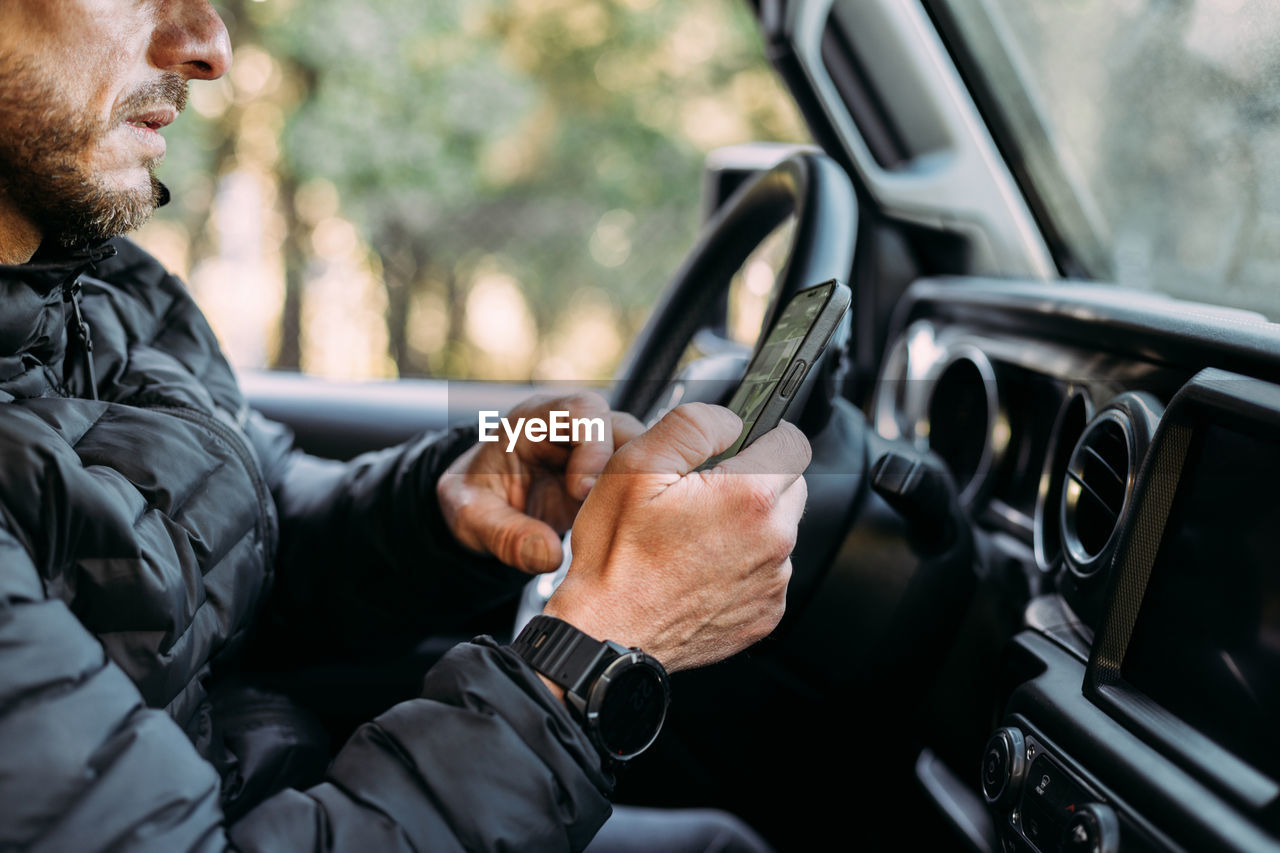 Crop view of unrecognizable man using his mobile inside the car before starting to drive