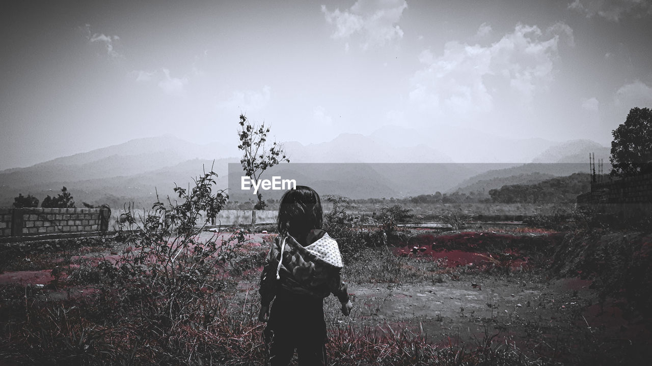 Rear view of girl standing on field against sky