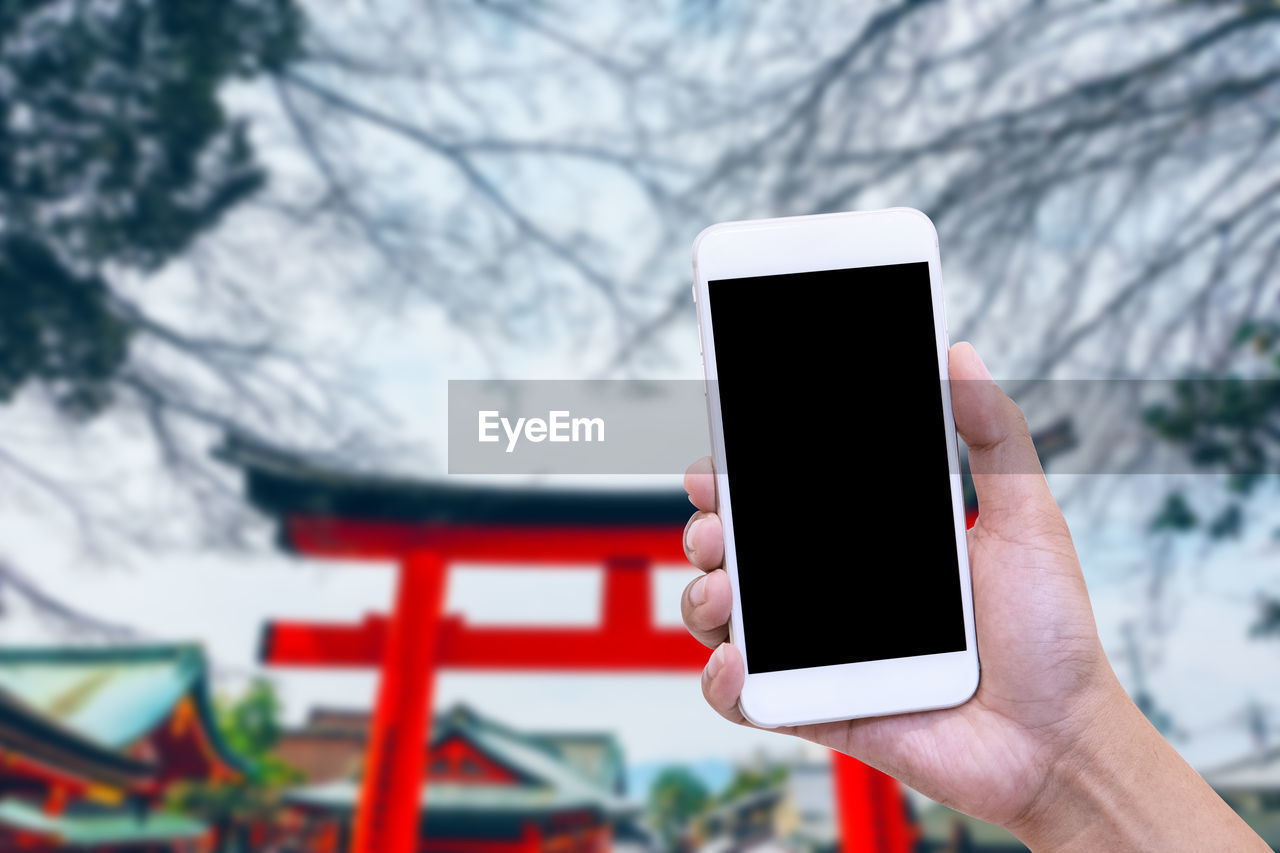 Cropped hand holding mobile phone against torii gate