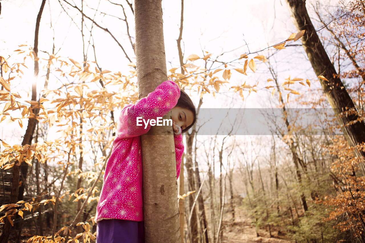Portrait of girl embracing tree trunk at yard during autumn